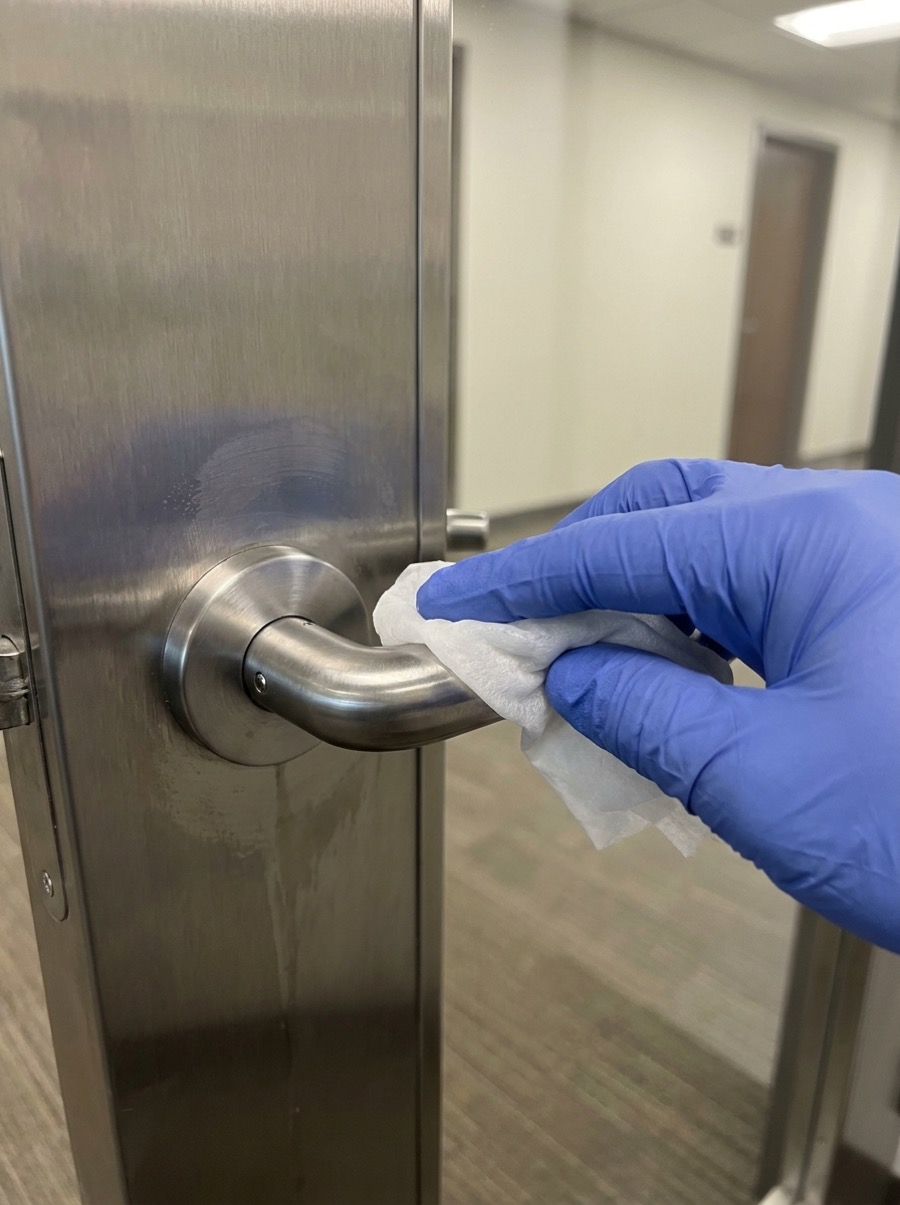 A gloved hand disinfecting a stainless steel door handle